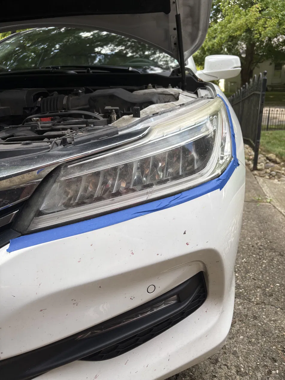 Hazy headlight lens masked with blue tape and frosted mid-restoration